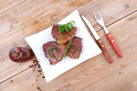 roasted beef meat strips steak on white ceramic plate with hot dry pepper on wood table