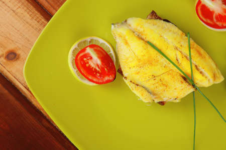 served roast golden fish fillet over wooden table with tomatoes and olivesの写真素材