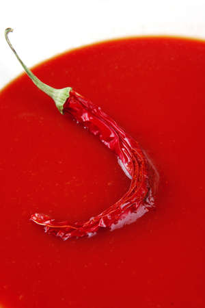 hot fresh diet tomato soup with basil thyme and raw tomatoes in white round bowl over red mat on...