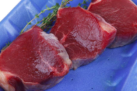uncooked raw beef fillet with thyme twig on blue tray isolated over white background