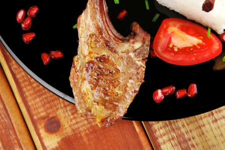 main course: grilled ribs with rice and tomatoes on black dish over woodの写真素材