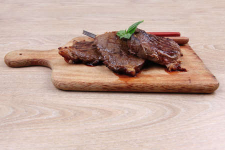 grilled beef on wooden plate with cutlery over table