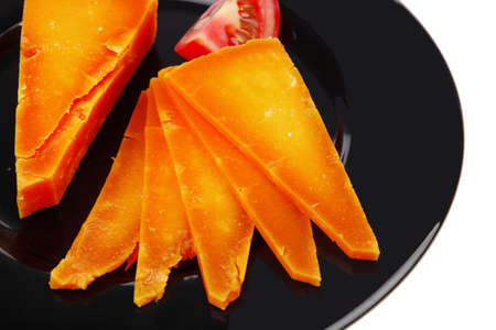 orange aged delicious cheddar cheese chop with slice and tomato on black plate isolated over white backgroundの写真素材