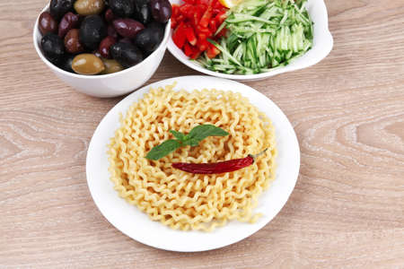 italian food : fresh pasta with basil leaf and red hot pepper on white dish over wooden tableの写真素材