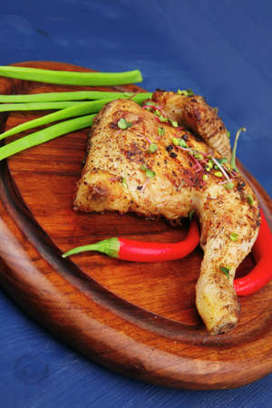 roast meat : chicken legs garnished with green onion pens and peppers on wooden plate over blue wooden backgroundの写真素材