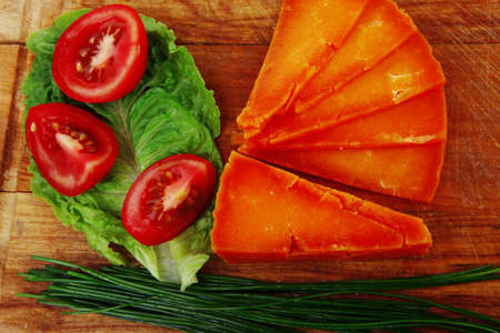 orange aged delicious cheddar cheese chop with slice on wooden plate with tomatoes , chives and salad . isolated over white backgroundの写真素材