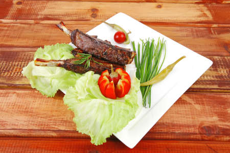 meat plate on wooden table: roast ribs on white with tomatoes and red hot peppers