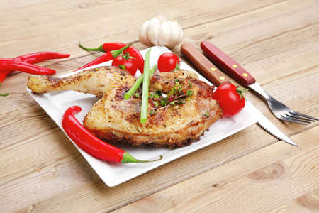 meat food : chicken legs garnished with hot chili peppers on white plates over wooden tableの写真素材