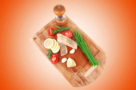 savory sea fish entree : roasted salmon fillet with green onion, red cherry tomatoes pieces, glass pepper grinder, rosemary twigs and lemon on wooden board isolated on white backgroundの写真素材