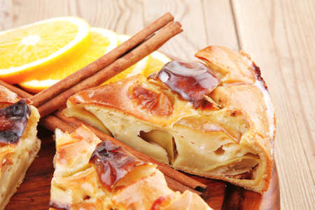 sweet food : cuts of apple pie on wooden plate with cinnamon sticks and lemonsの写真素材