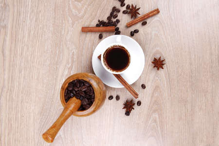 sweet hot drink : black arabic coffee in small white cup with mortar and pestle , beans spilled over wooden table , decorated with cinnamon sticks and anise starsの写真素材