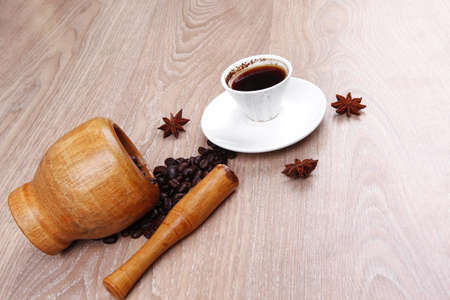 sweet hot drink : black arabic coffee in small white cup with mortar and pestle , beans spilled over wooden table , decorated with cinnamon sticks and anise starsの写真素材