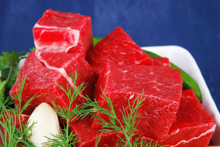 uncooked fresh beef meat chunks on white bowls with green hot peppers and vegetables serving over...