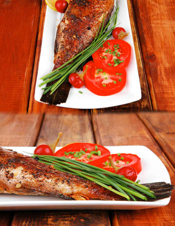 whole fried bass on plate over wood, served with lemons and tomatoes