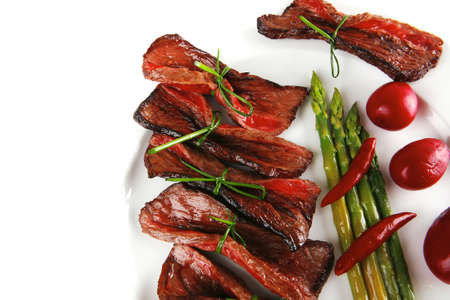 curved meat slices on white dish with vegetablesの写真素材