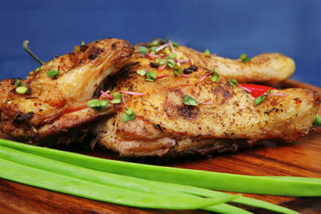 meat food : roasted chicken legs garnished with green onion pens and peppers on wooden plate over blue wooden backgroundの写真素材