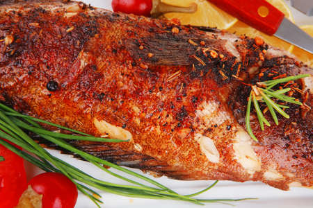 savory isolated on white: whole fryed sunfish over plate with tomatoes lemons and peppers