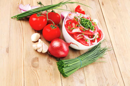 healthy appetizer : fresh tomato salad in white bowl with bunch of chives and raw tomatoes on twig , violet onion, garlic over wooden tableの写真素材