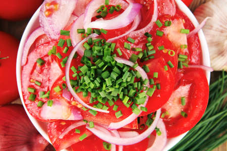 healthy food : fresh tomato salad in white bowl with bunch of chives and raw tomatoes on twig , onion, and garlic over wooden tableの写真素材