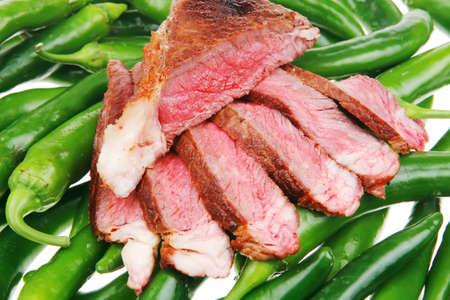 meaty food : grilled red meat steak sliced on a green hot chili peppers on a white back backgroundの写真素材