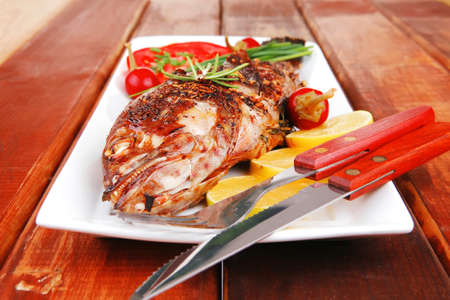 main course on wood: whole fryed sunfish on plate with lemons and peppers