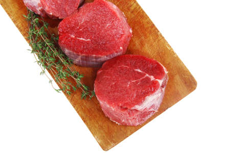 red raw fillet chops : three fresh beef meat chops with thyme twig on wooden plate . isolated over white backgroundの写真素材