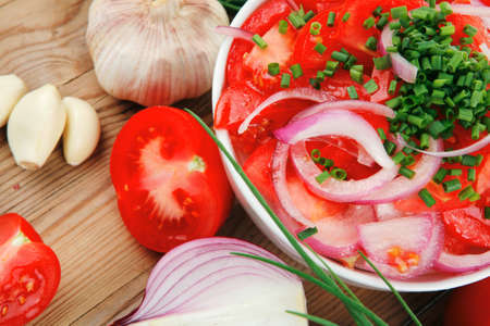 vegetable salad : fresh tomato salad in white bowl with bundle of chives , tomatoes on twig , onion, and garlic over wooden tableの写真素材