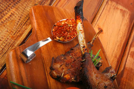 meat savory on wooden plate: roast ribs with peppers tomato and dry spices over wooden tableの写真素材