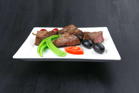 meat food : roasted fillet mignon on white plate with tomatoes apples and chili pepper over black wooden tableの写真素材
