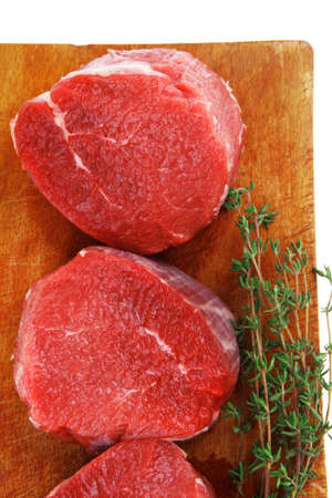red raw fillet chops : three fresh beef meat chops with thyme twig on wooden plate . isolated over white backgroundの写真素材