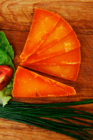 orange aged delicious cheddar cheese chop with slice on wooden plate with tomatoes , chives and salad . isolated over white backgroundの写真素材