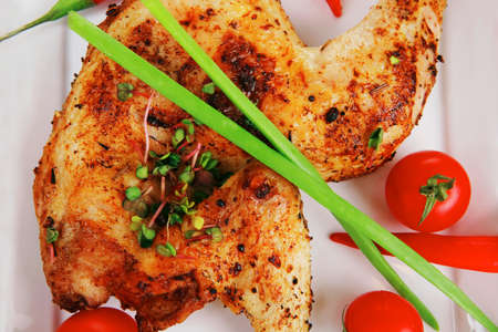 meat : chicken quarters garnished with red hot peppers on white plates over wooden tableの写真素材