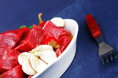 raw fresh beef meat slices in a white bowls with onion and red peppers serving on blue table with cutleryの写真素材