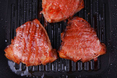 fresh grilled bloody beef steaks on black grill plate isolated on white background