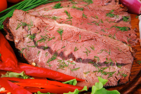 beef slices on wooden plate with peppers on wood