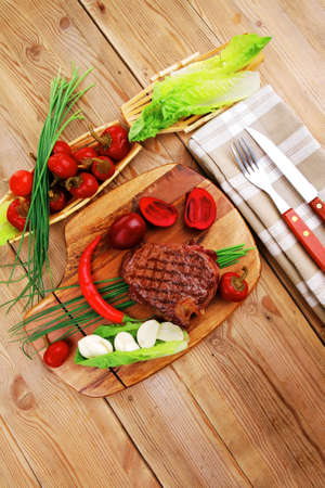 meat food : roast beef garnished with green staff and red chili hot pepper on wooden table with cutleryの写真素材
