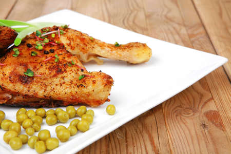 grilled meat : grilled quarter chicken garnished with green sweet peas , red peppers on white plates over wooden tableの写真素材