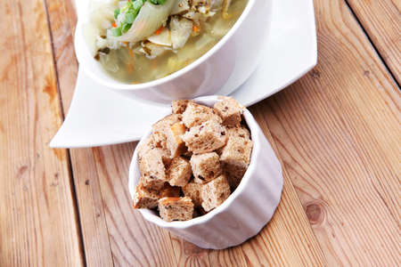 hot fresh diet vegetable soup with rye bread crackers over wood table on white ceramic standの写真素材