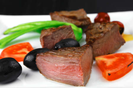 meat savory : grilled beef fillet mignon on white plate with tomatoes apples and pepper over black wooden tableの写真素材