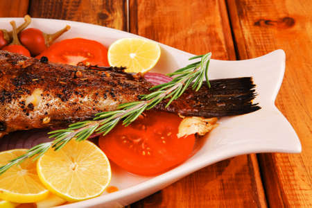 main course: whole fried seabass served on wood with lemons,tomatoes and peppersの写真素材