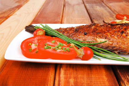 main course on wood: whole fryed sunfish on plate with lemons and peppersの写真素材