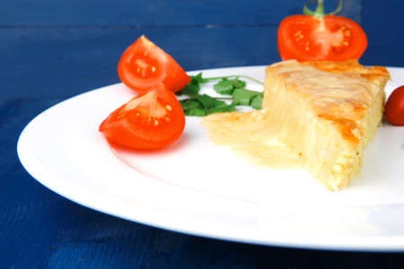 food : cheese casserole piece on white plate served with parsley and tomatoes on blue tableの写真素材