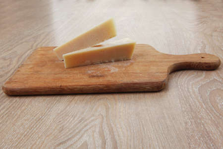 two fresh triangle french delicacy parmesan cheese pieces on wooden cut board over table
