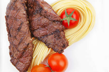 grilled beef fillet with pasta and tomatoes on white plate isolated over white backgroundの写真素材