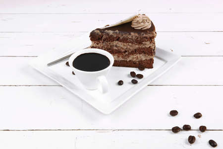 breakfast hot coffee mug and cream chocolate layer cake decorated with white chocolate slice and cream flower on white plate over woodの写真素材