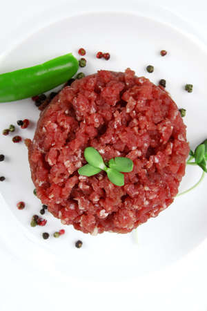 very big raw hamburger cutlet with sprouts and chilli pepper on white plate isolated over white backgroundの写真素材