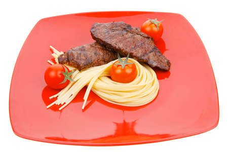 meat grilled beef steak with pasta and tomatoes on red plate isolated over white backgroundの写真素材