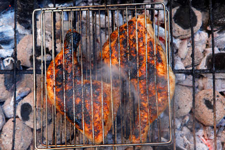 grilling spiced chicken in grid on charcoal bbq with tomatoes and vegetables