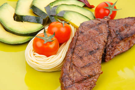 grilled meat beef steak with pasta avocado and tomatoes on green plate isolated over white backgroundの写真素材
