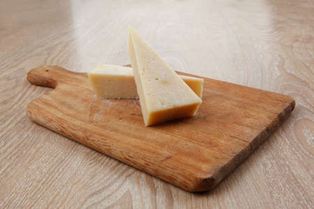 two fresh triangle french delicacy parmesan cheese pieces on wooden cut board over table